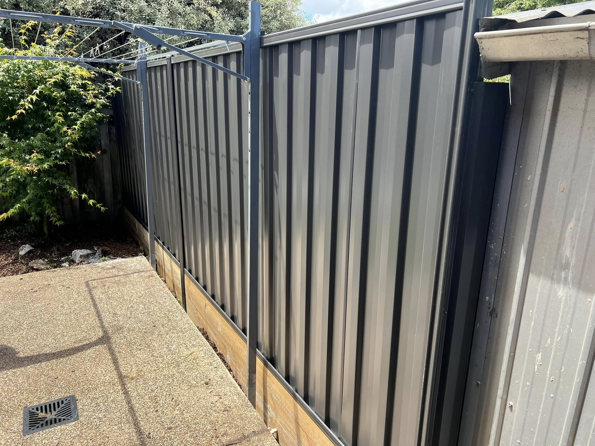Charcoal Colorbond steel fence panels along a paved side path