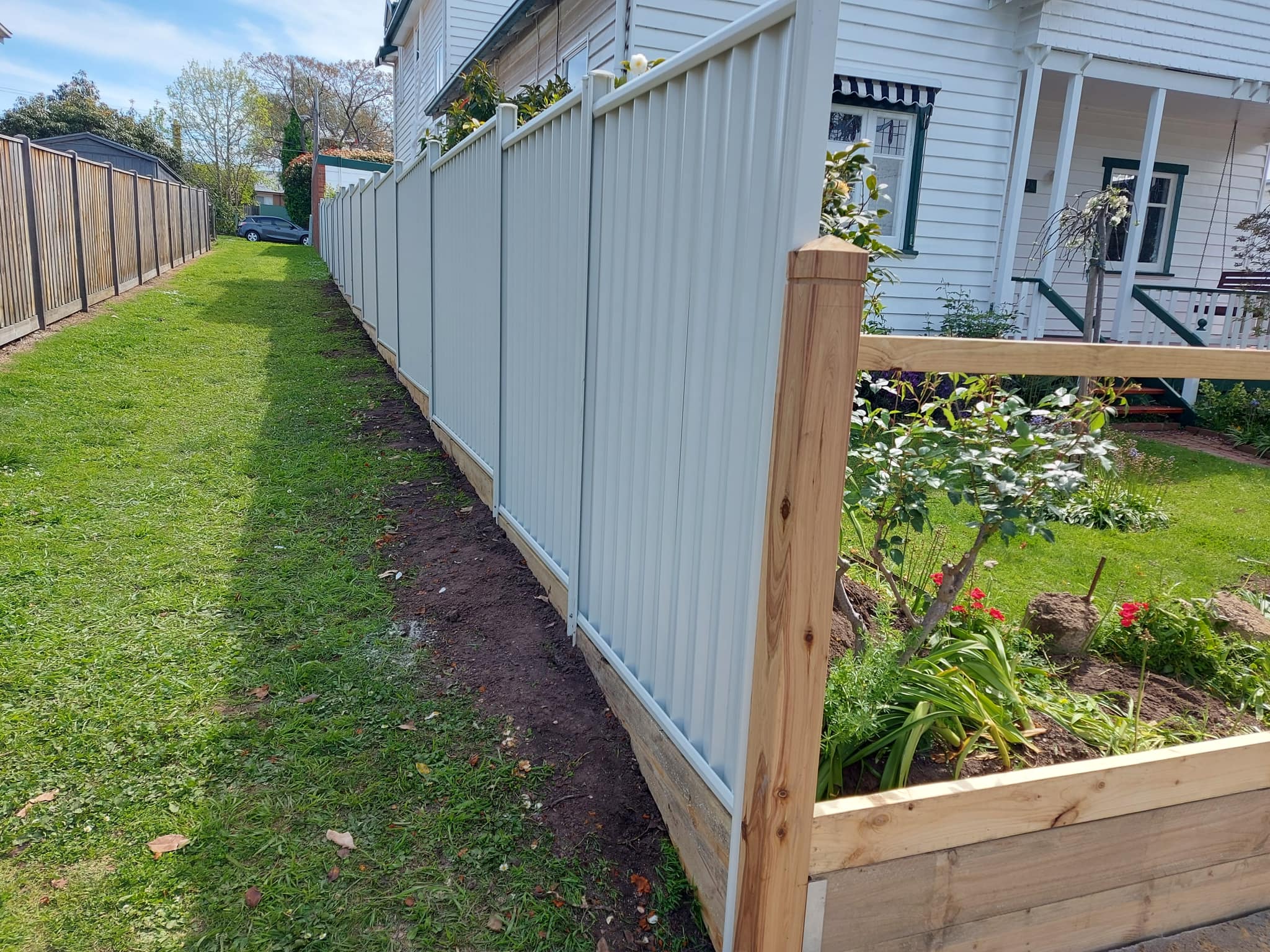 White Colorbond fence panels next to a heritage weatherboard cottage