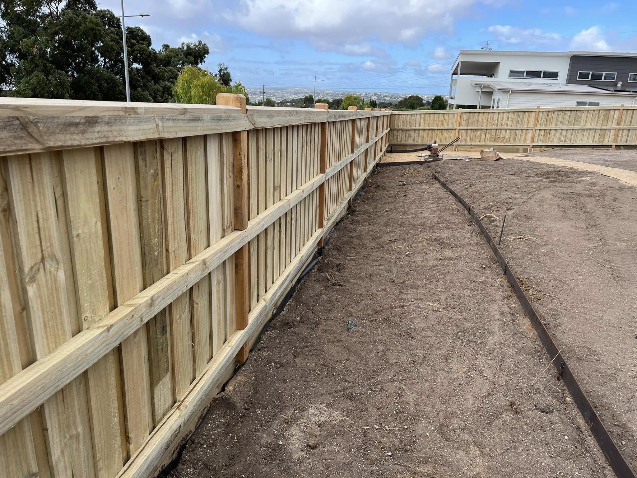 Capped paling fence wrapping around a new-build block with hilltop views