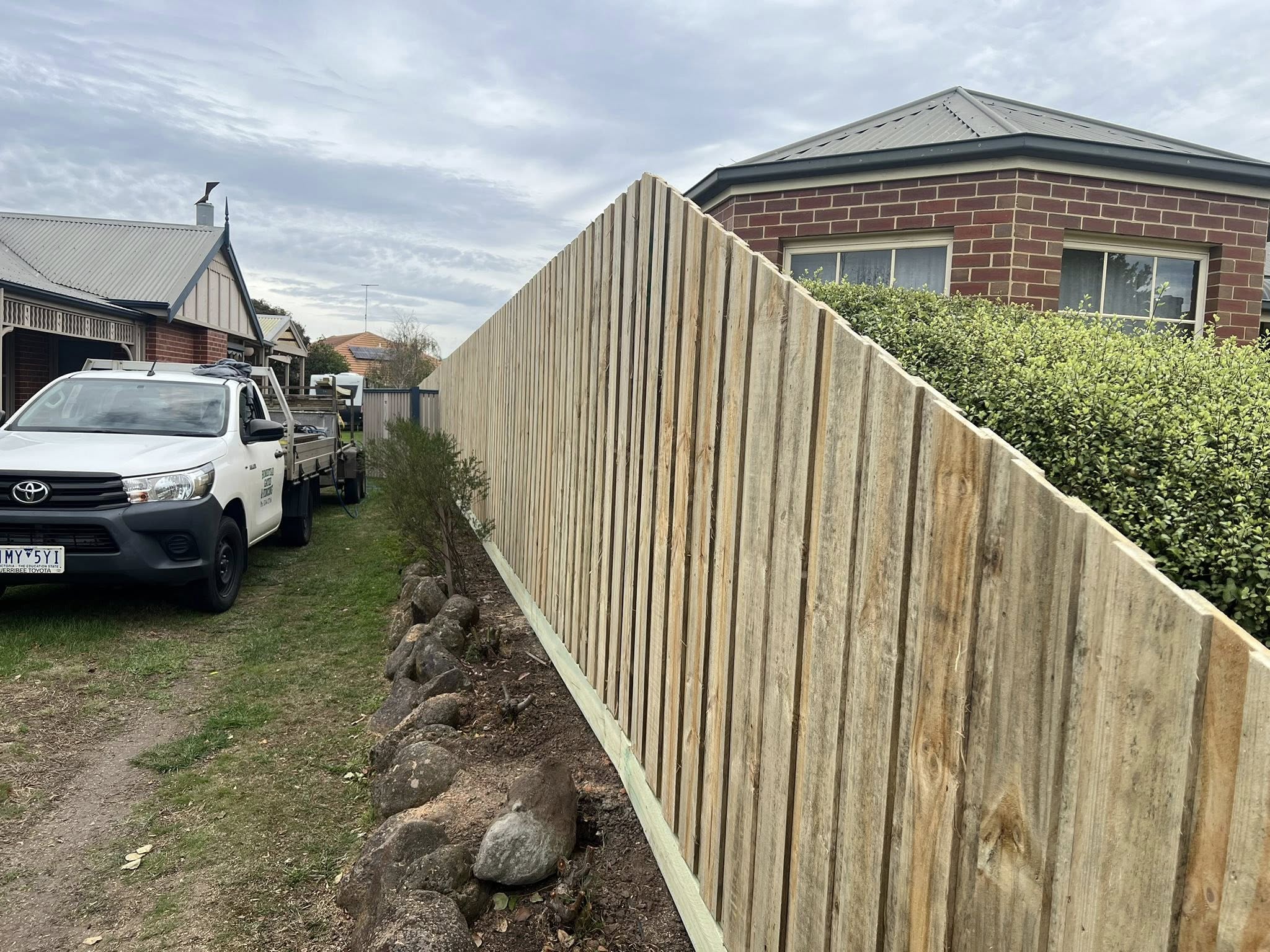 Tall vertical capped paling fence along a driveway